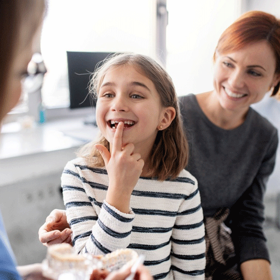 A young girl pointing to her teeth in a dentist's office.